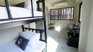 A bunk bed room with a desk and a chair, an air conditioning unit, and a window with bars.