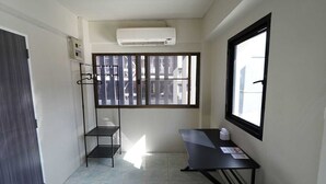 A small, well-lit room with a window, a desk, a chair, and a hanging coat rack.