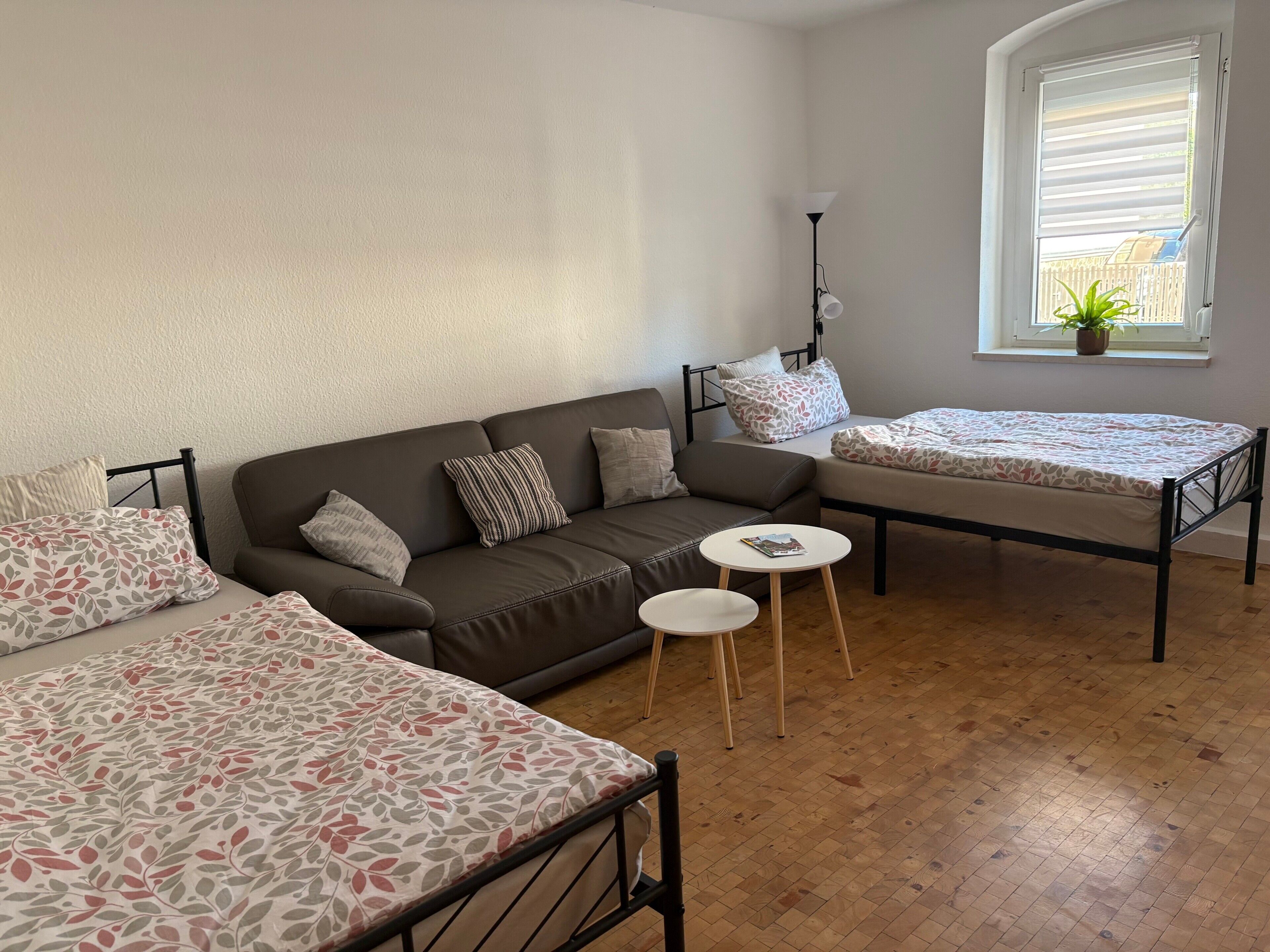 Ett rum med en soffa, en säng, ett litet bord och ett fönster med persienner.