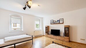 A bedroom with two beds, a TV, wooden furniture, and framed pictures on the wall. - Apartment 'Weida' with Wi-Fi (Riesa)