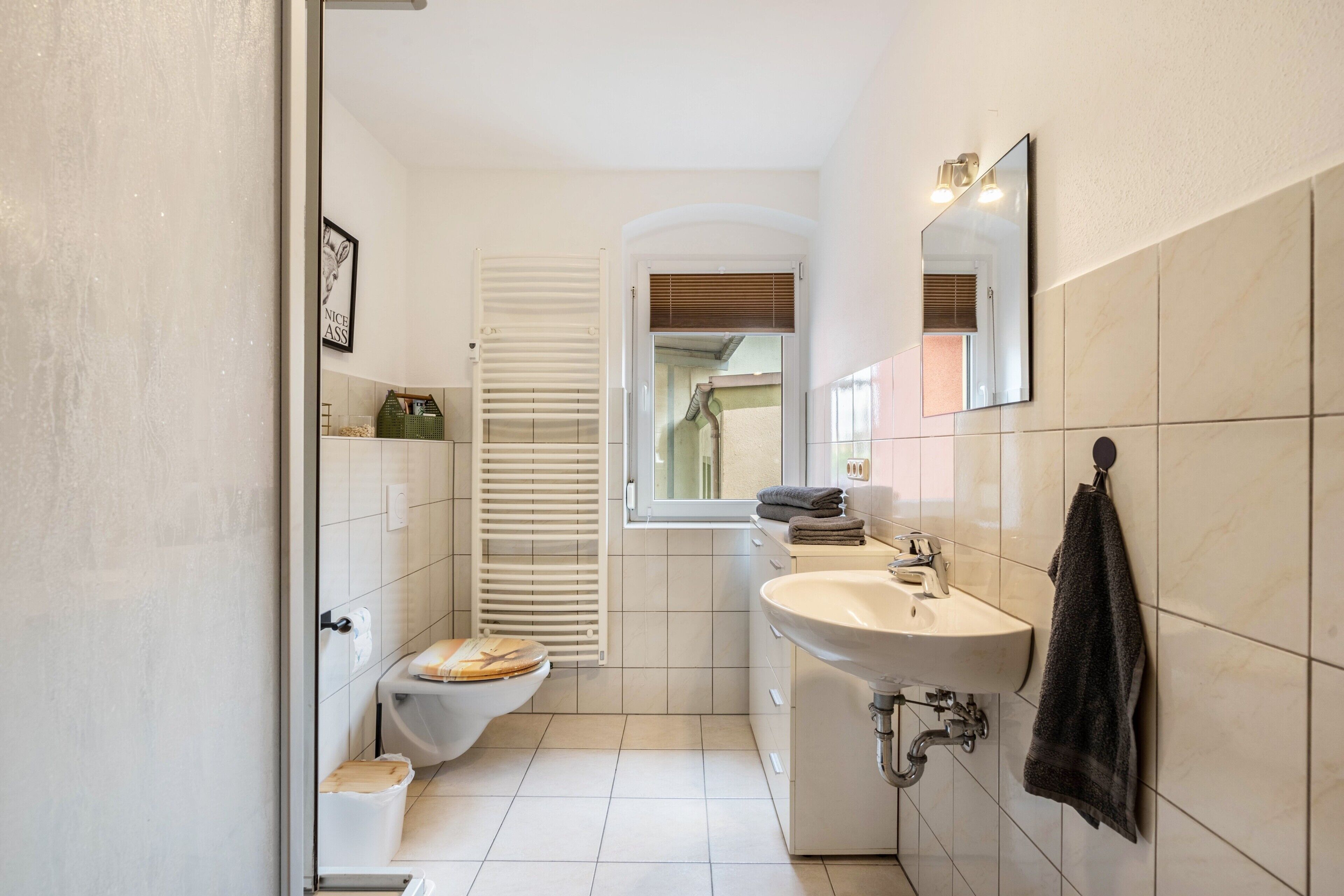 Un baño con inodoro, lavabo, espejo, toallero y una ventana con persianas.
