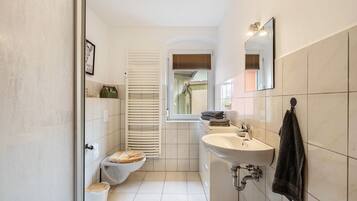 Un baño con inodoro, lavabo, espejo, toallero y una ventana con persianas.