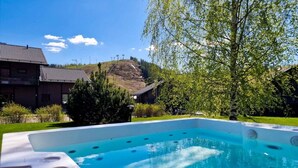 A rectangular hot tub with a clear blue pool, surrounded by a grassy area with trees and a building in the background. - Villa Kastanja, Himoslaakso Ski-in/out (Keski-Suomi)