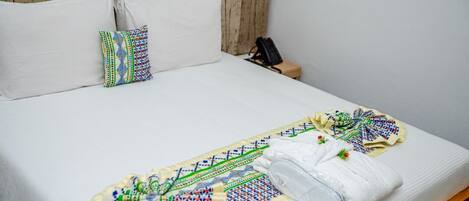 A neatly made bed with white linens, a colorful embroidered pillow, and a folded white towel on the bed.