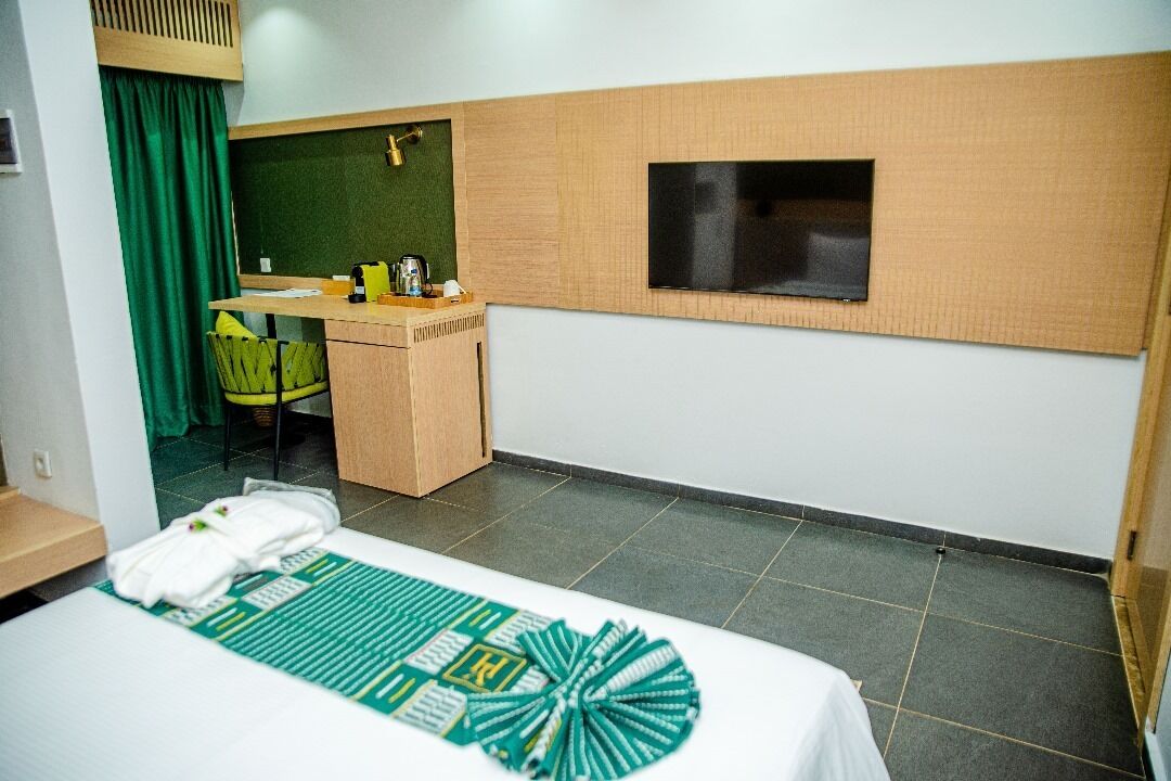 A hotel room with a bed, a desk, a chair, a television, and a green curtain.