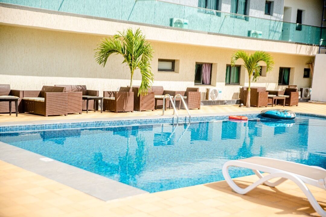 A swimming pool with lounge chairs and palm trees, surrounded by a building with balconies.