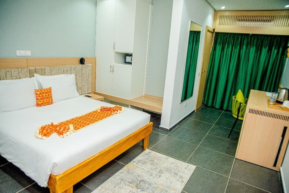 A hotel room with a bed, a wooden bench, a desk, and a green curtain.