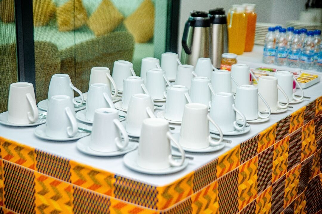 Montaje de un bufé de desayuno con varias tazas y platillos blancos, una cafetera y botellas de agua.