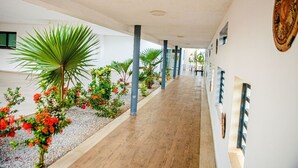 A corridor with a wooden floor, white walls, and decorative plants. - HOTEL YATCHENIN YAMOUSSOKRO (Yamoussoukro)
