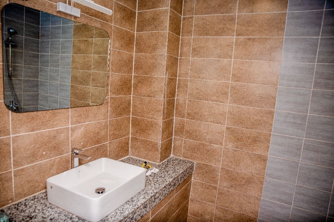 A bathroom with a white sink, a mirror, and brown tiled walls.
