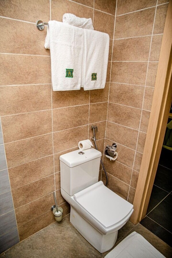 A bathroom with a toilet, a towel rack with two towels, and a toilet paper holder. - HOTEL YATCHENIN YAMOUSSOKRO (Yamoussoukro)