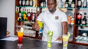 A bartender preparing drinks at a bar with a variety of bottles and glasses in the background. - HOTEL YATCHENIN YAMOUSSOKRO (Yamoussoukro)