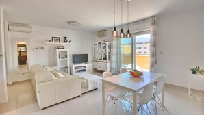A modern living room with a sofa, TV, dining table, and chairs. - All-inclusive penthouse with views in Denia (Denia)