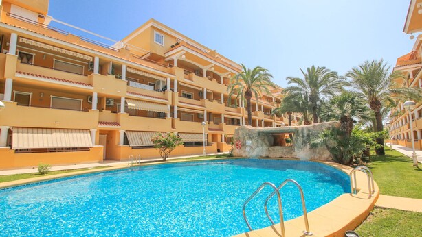 A swimming pool surrounded by multi-story buildings with balconies, palm trees, and a clear blue sky. - All-inclusive penthouse with views in Denia (Denia)