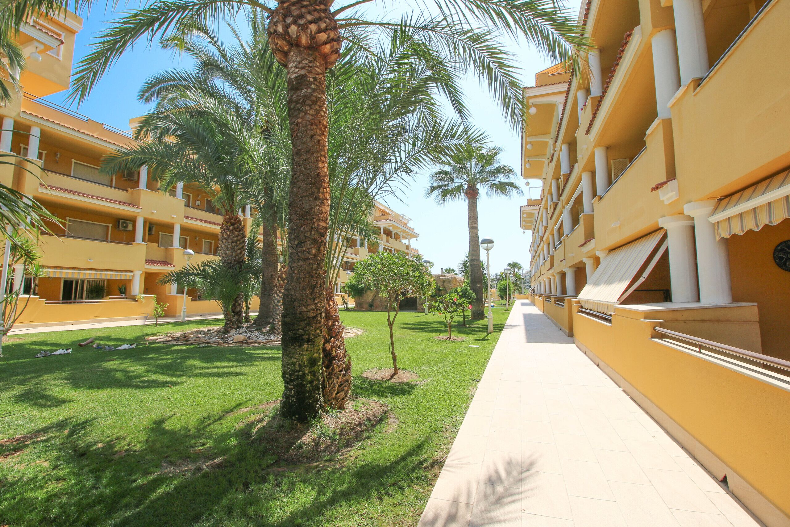 A yellow building with balconies and palm trees.