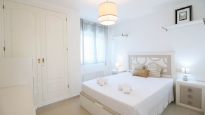 A bedroom with a bed, bedside tables, a nightstand, a hanging light, a window with curtains, and a door. - All-inclusive penthouse with views in Denia (Denia)