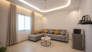 Uma sala moderna com sofá seccional, uma mesinha de centro redonda, geladeira e micro-ondas.