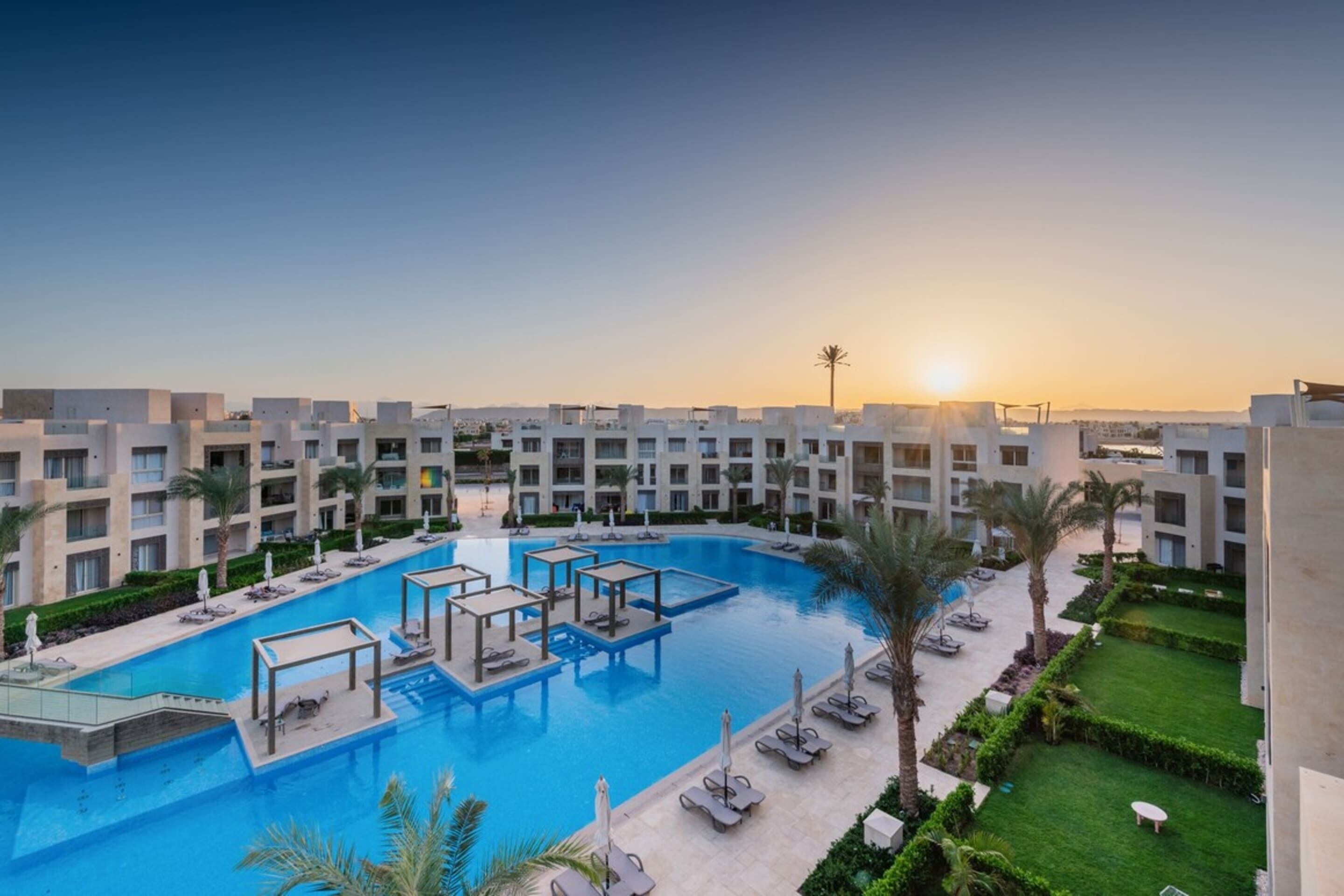 A resort with a central swimming pool, multiple balconies, and palm trees.