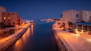 A marina at dusk with boats docked, a stone pathway, and buildings with warm lighting.