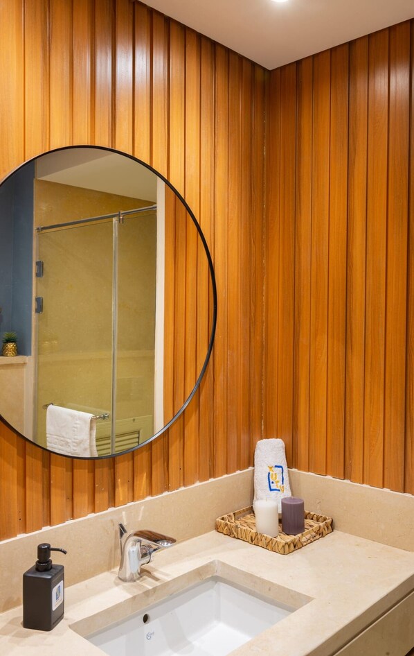 Une salle de bain avec un mur recouvert de panneaux en bois, un miroir rond, un lavabo et une douche.