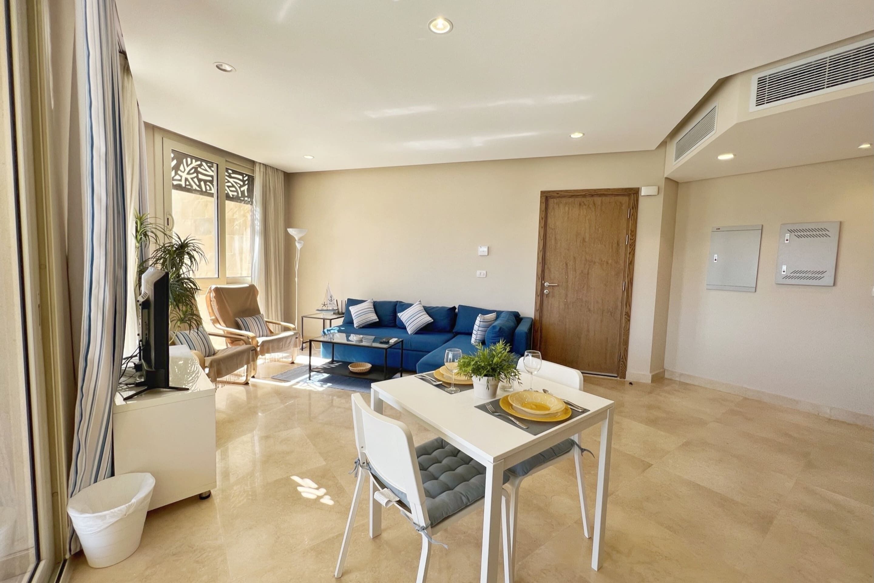 Una sala moderna con un sofá azul, una mesa de comedor blanca y una pequeña mesa blanca con una planta.
