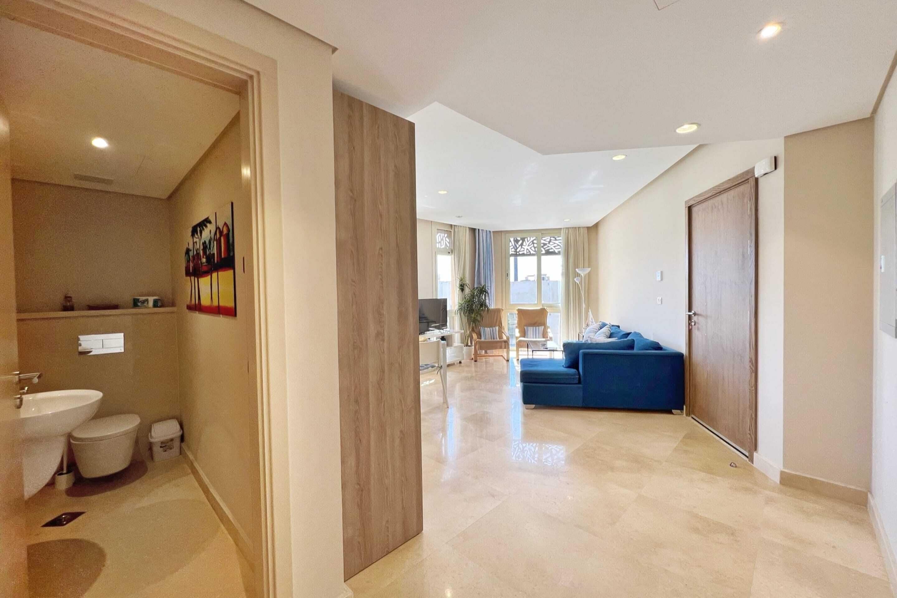 A modern interior with a bathroom, a living area with a blue sofa, and a dining area with a table and chairs.