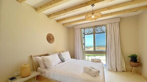 A bedroom with a wooden bed, a bedside table with a lamp, a window with curtains, and a view of the outdoors.