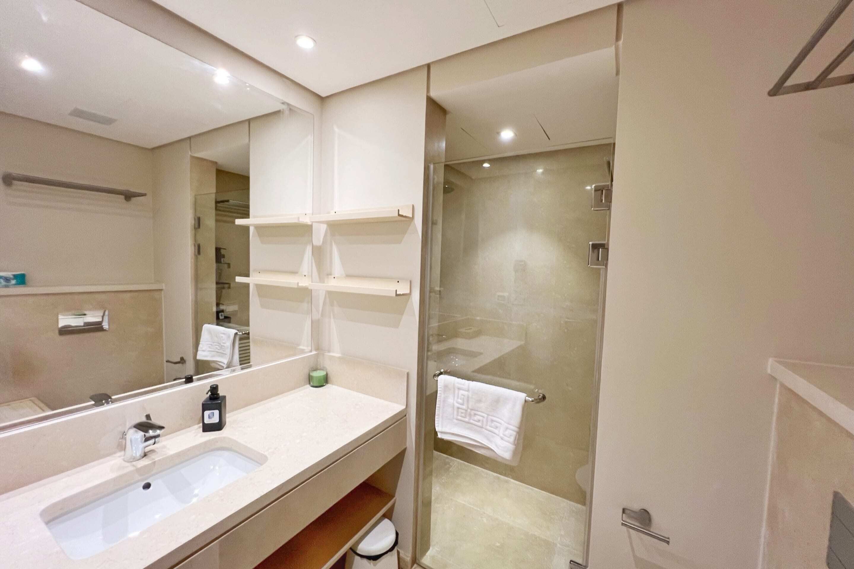 A modern bathroom with a large mirror, a sink, a glass shower enclosure, and a towel rack.