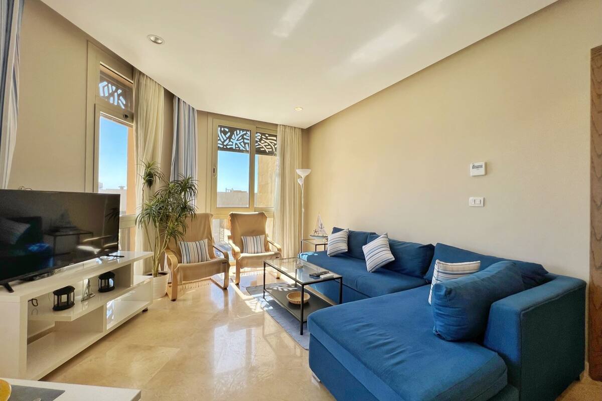 Un salon moderne avec un grand téléviseur à écran plat, un canapé bleu, une table basse et une plante en pot.
