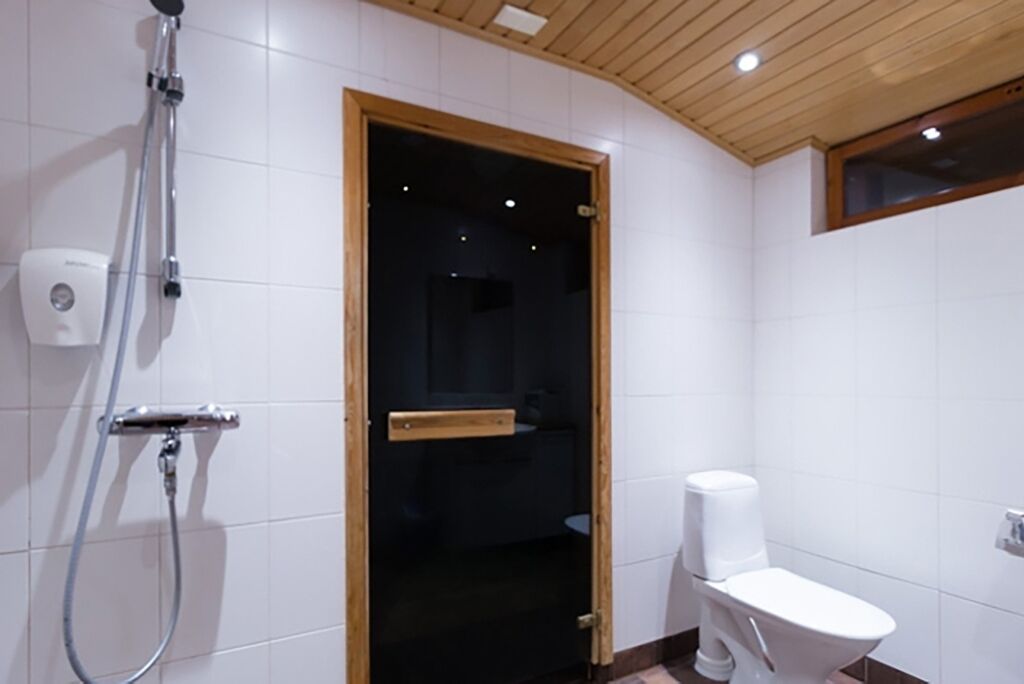A bathroom with white tiles, a shower, a toilet, and a wooden door.