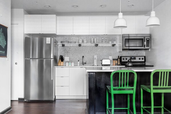 Eine moderne Küche mit Edelstahlgeräten, weißen Schränken und grünen Barhocker.