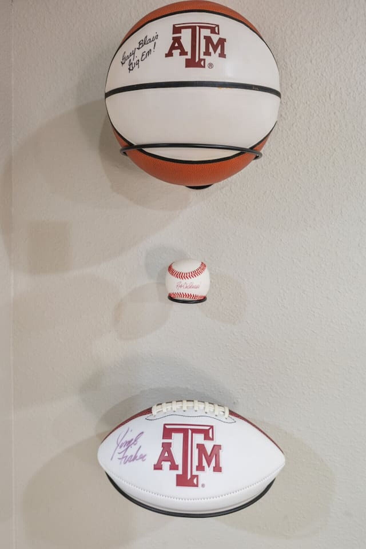 Un ballon de football et une balle de baseball, tous deux ornés du logo de l’université Texas A&M, et fixés au mur.
