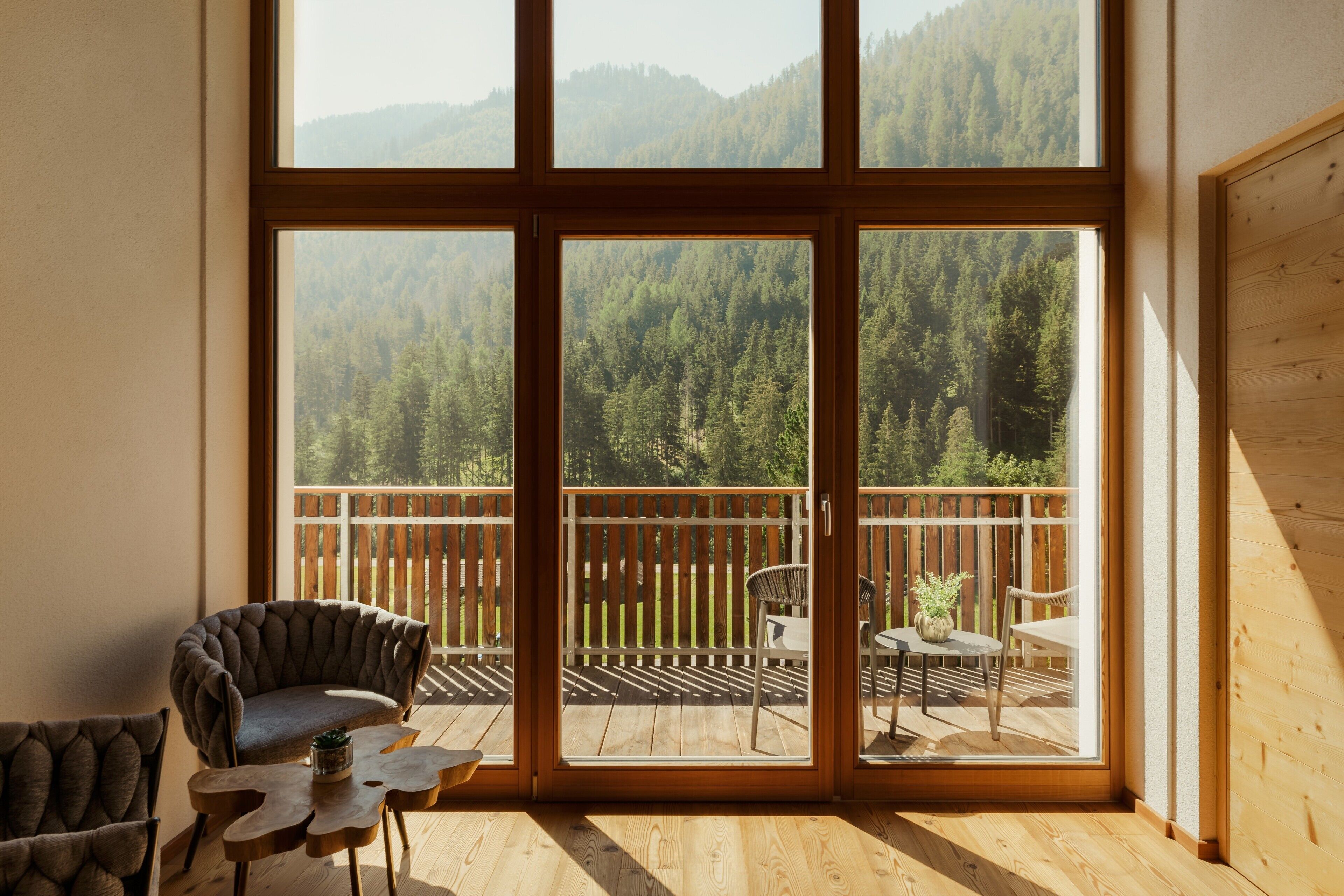 A room with a large sliding glass door leading to a balcony with a wooden deck and chairs.
