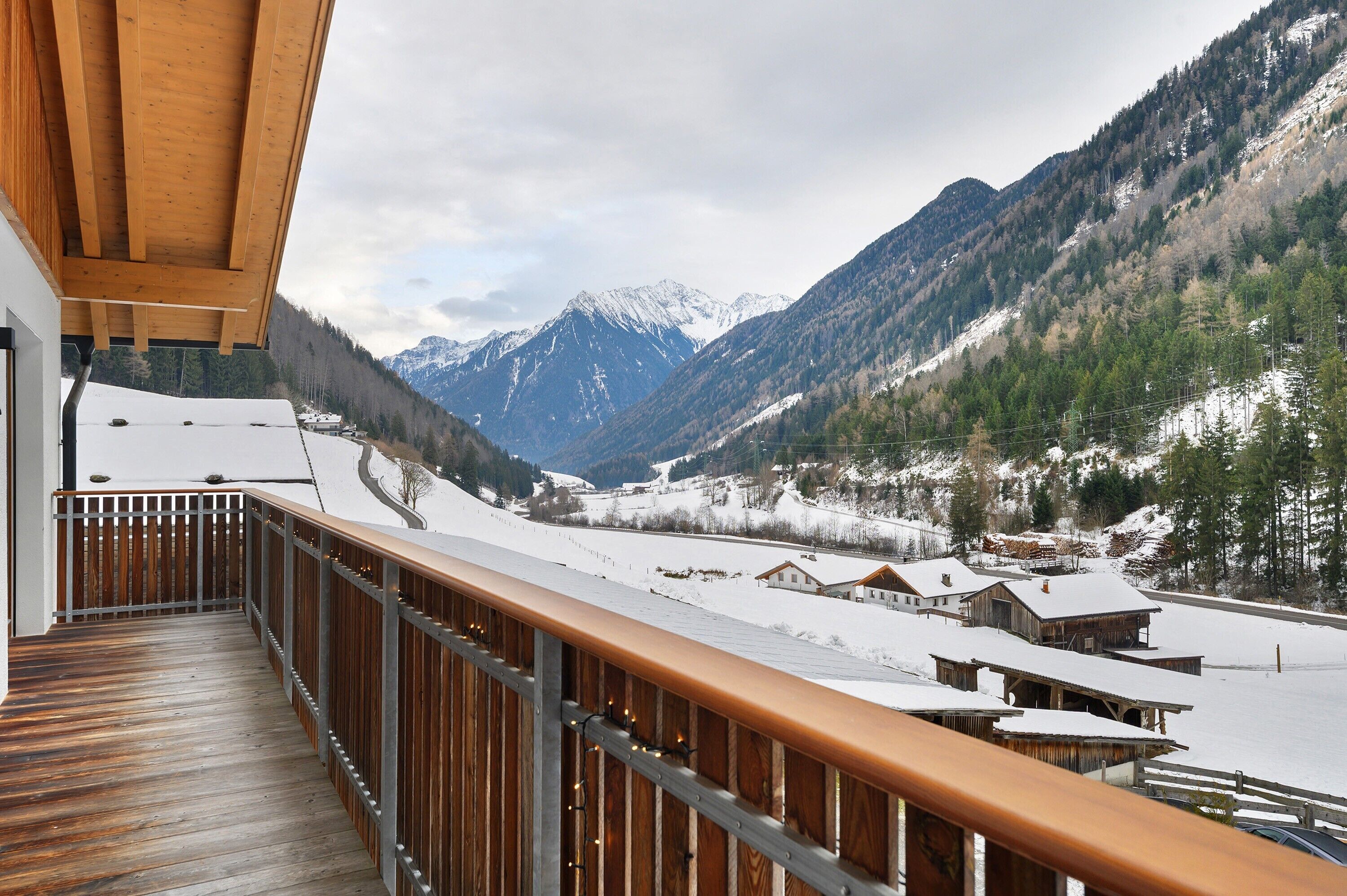 Un terrazzo in legno con vista su montagne innevate e edifici.