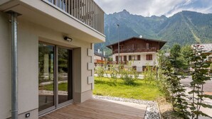 Ein modernes Gebäude mit einer Holterrasse, großen Glasüren und Blick auf ein Gebirge.