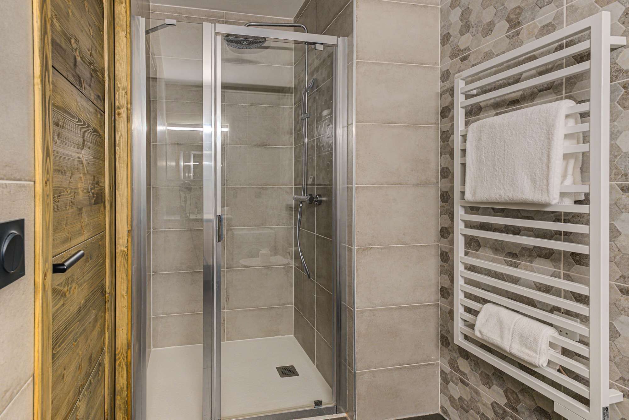 Een douche met glazen deur, een handdoekhouder met handdoeken, en een houten deurkozijn.