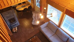 A cozy cabin interior with a fireplace, a sofa, a dining table, and a large window. - Villa Slalom 2, Himos Länsihuippu (Keski-Suomi)