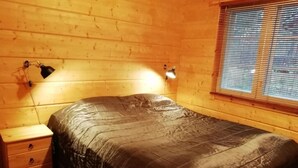 A wooden cabin room with a bed, a nightstand, and a window with blinds. - Villa Slalom 2, Himos Länsihuippu (Keski-Suomi)