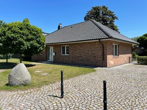 A brick house with a tiled roof, a paved driveway, and a stone sculpture in the foreground. - Holiday Home 'Ferienhaus Rechlin' with Private Terrace, Private Garden and Wi-Fi (Rechlin)