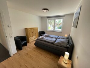 A bedroom with a bed, a wardrobe, a chair, a bedside table with a lamp, and a window. - Holiday Home 'Ferienhaus Rechlin' with Private Terrace, Private Garden and Wi-Fi (Rechlin)