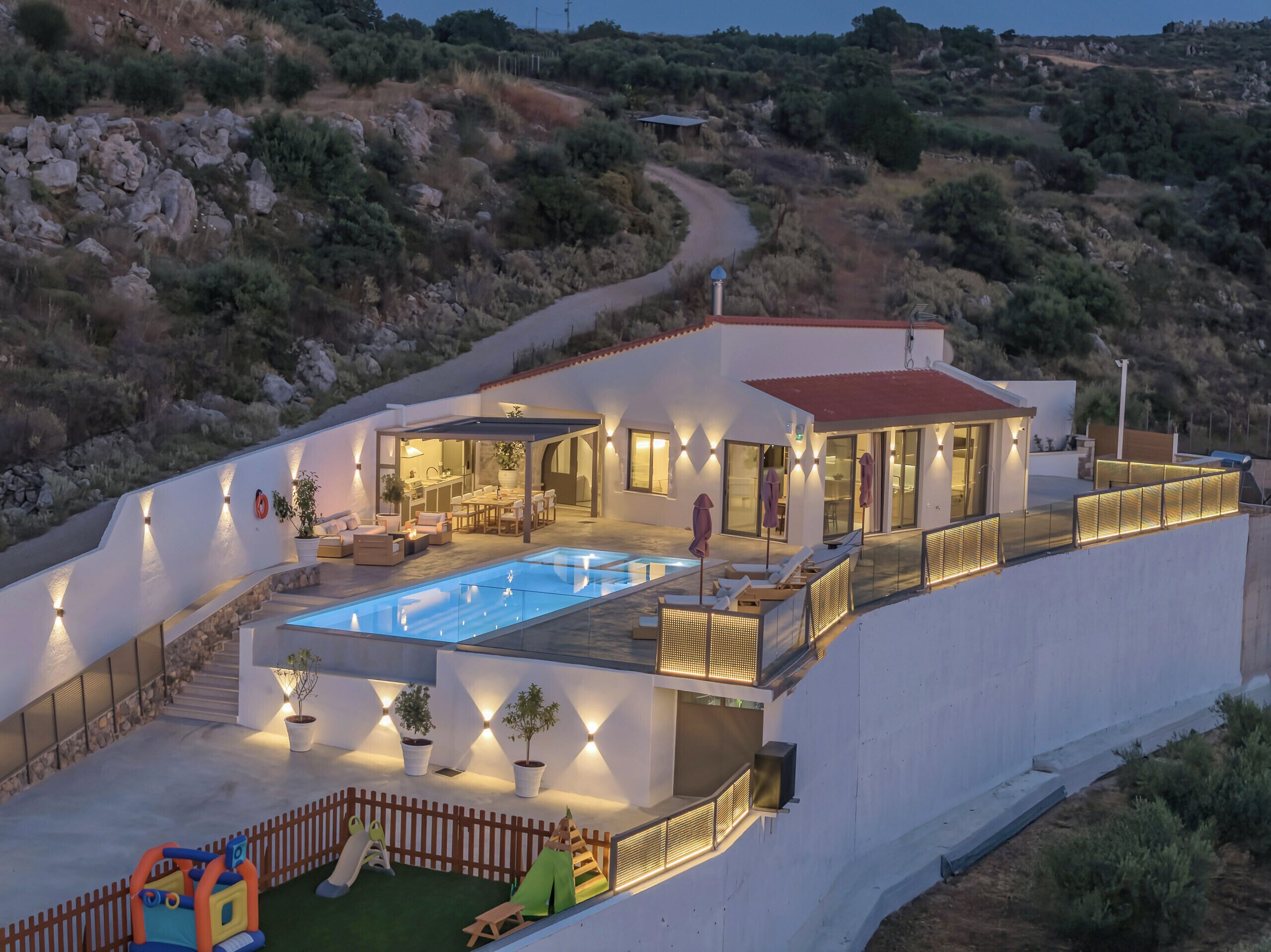 A modern villa with a swimming pool, outdoor seating, and a scenic hillside view.
