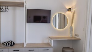 Une chambre moderne dotée d’un téléviseur à écran plat fixé au mur, d’un miroir rond avec éclairage intégré, d’une console en bois et d’un petit tabouret.