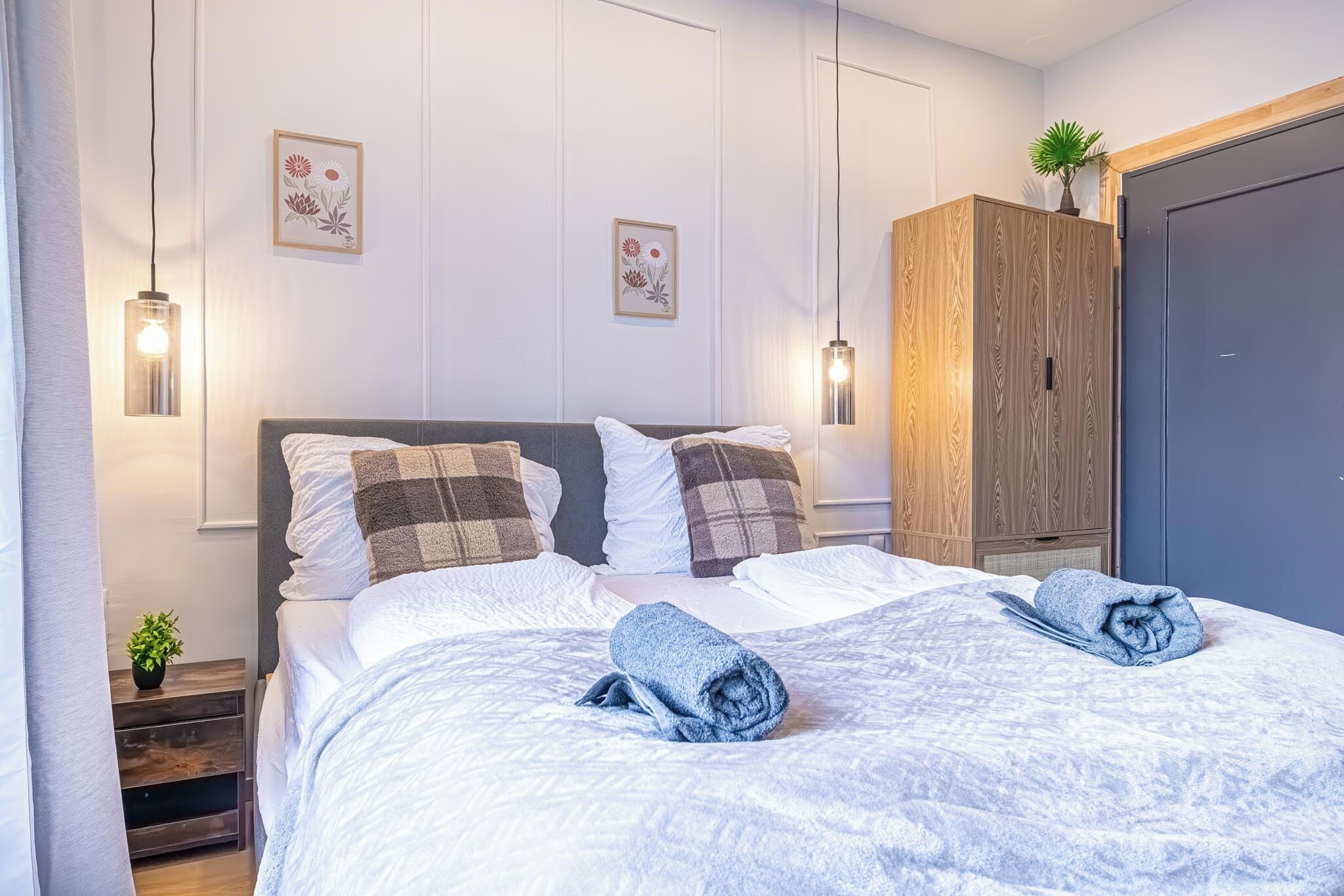 A neatly made bed with a blue towel, a wooden wardrobe, and wall-mounted lights.