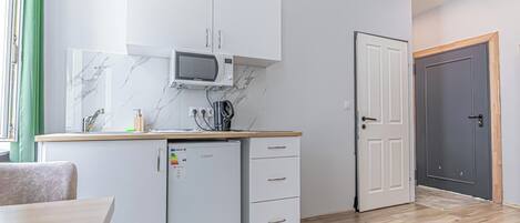 Eine kompakte Küche mit weißen Schränken, einer Mikrowelle, einem kleinen Kühlschrank und einer Holz Arbeitsplatte.