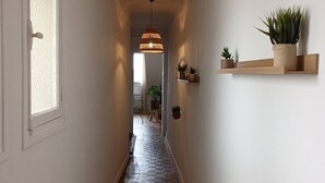 A narrow hallway with wooden flooring, a hanging pendant light, and a wooden shelf with potted plants.