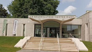 The entrance to Le Quadrilatère Centre D'Art, featuring a modern architectural design with a glass facade and a set of stairs leading up to the entrance.