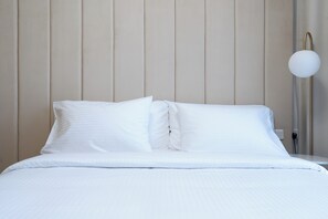 Ein ordentlich bezogenes Bett mit weißen Leinen in einem Zimmer mit Holzpaneelen und einer modernen Stehlampe.