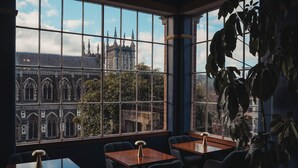 Une pièce dotée de grandes fenêtres, offrant une vue sur un bâtiment historique, et agrémentée d’une grande plante.