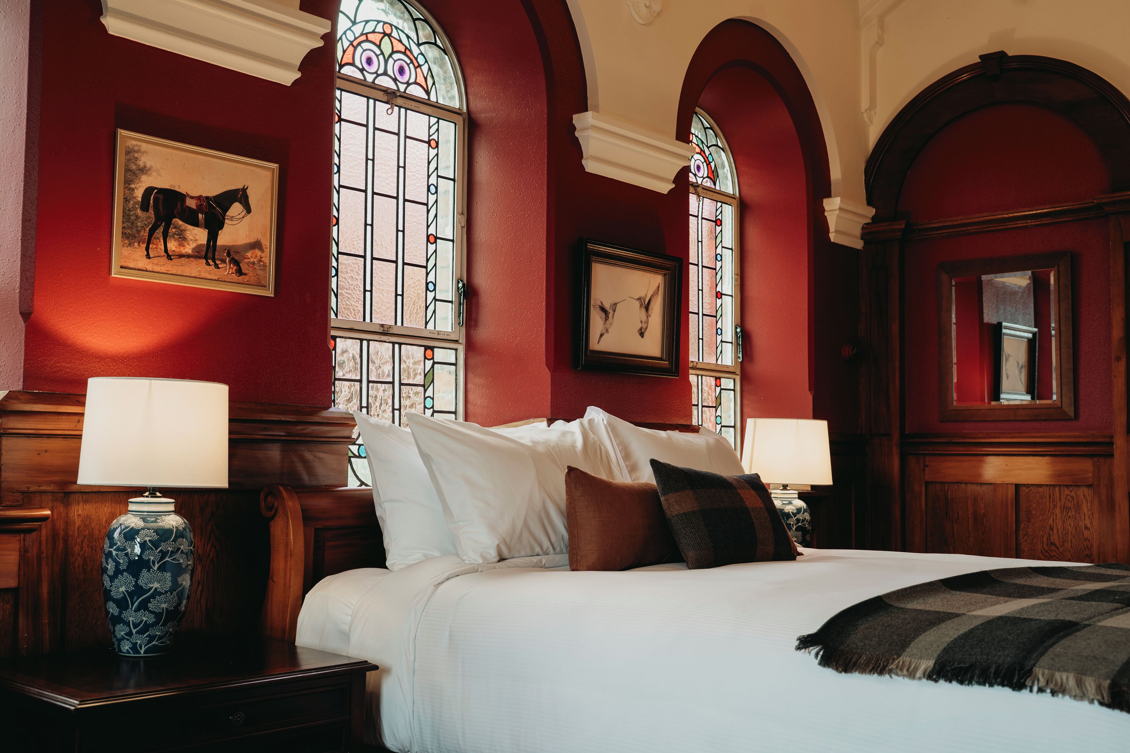 A hotel room with a large bed, two nightstands, a vase, and two framed pictures on the wall.