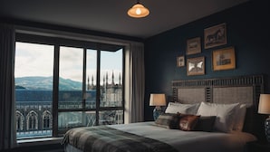 Une chambre avec une grande fenêtre, un lit avec des oreillers et une tête de lit ornée de tableaux encadrés.